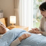 スイトルボディによる清潔ケアで肌トラブルを防ぎ、寝室で安らかに眠る高齢女性と、その傍らで優しく見守る介護者の様子